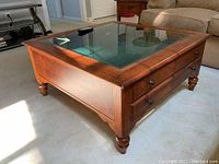 Angled view of coffee table showing wood finish, glass top, and turned wooden legs.