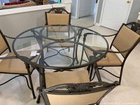 Full set of the Ethan Allen round metal table with glass top and four matching metal chairs with upholstered seats shown in room with white walls and floor.