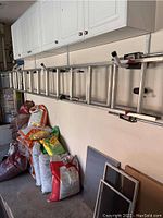 Aluminum ladder mounted horizontally on garage wall above bags of soil and supplies