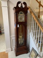 Full front view of the grandfather clock showing complete wood case, glass panels, brass weights and pendulum.