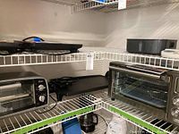 Wire shelving with top shelf bakeware and griddle, bottom shelf showing Oster toaster oven (left) and stainless toaster oven (right).