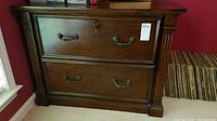 Front view of the dark wood lateral file cabinet showing two large drawers with metal handles and keyholes, slight surface wear visible.