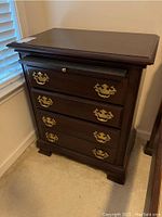 Full view of the dark wood nightstand showing four drawers with brass escutcheon handles and pull-out tray.