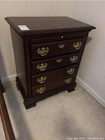Front angle view of Kincaid wood nightstand showing four drawers with brass hardware, pull-out tray, and bracket feet.