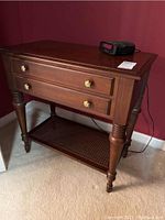 Front right angle view of wooden nightstand with two drawers and lower cane shelf.