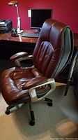 Side view of brown faux leather executive office chair showing cushioning and armrests.
