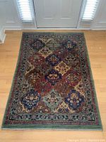 Full view of rectangular blue, green, burgundy patterned tapestry area rug on hardwood floor, showing diamond and floral design with border.