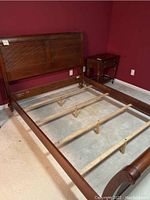 Full view of wooden queen size sleigh bed frame with headboard and footboard in a reddish-brown finish. Shows side rails and support slats in place but no mattress.