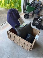 Lot showing beige storage container holding camping gear, blue tent bag, green pouch, and black fan in background