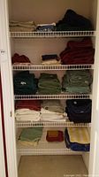 Closet with five wire shelves holding folded towels and linens in various colors and types, including bath towels, bedsheets, and pillowcases.