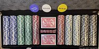 Poker chips in assorted colors (blue, green, red, white, black), two decks of cards, red dice, and large dealer chips arranged inside an aluminum case.