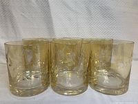 Group of six glasses with a golden tint and etched leaf design.