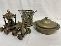 Photo of three antique brass items including a decorative chariot missing one rear wheel, a lidded covered dish, and a filigreed container with handles