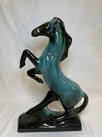 Front-right view of glossy blue-green and black rearing stallion horse ceramic statue showing details of mane, lifted front legs, and base.