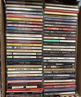 Photo of a vertical stack of approximately 50 music CDs in jewel cases showing a wide variety of artists and genres including punk, rock, compilations and alternative music.