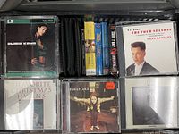 Mixed genre CDs including classical, jazz, and Christmas hymns along with audiobook cases stacked in a container.