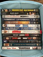 Photo showing 14 DVD movie cases stacked inside a box, titles visible on spines.