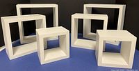 Front view of two sets of three white square floating shelves arranged side by side.