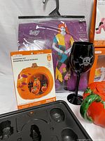 Photo showing adult XL costume in packaging, pumpkin diorama kit, black wine glass with spider design, orange/red wig