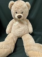 Front view of large beige plush teddy bear with ribbon on neck