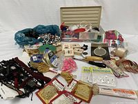 Wide angled photo showing an assortment of sewing accessories including ribbons, clasps, pearls, hooks and other crafting and sewing items all spread out on a white background.