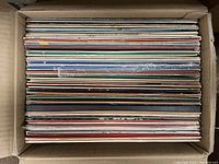 Box filled with vinyl records stacked vertically, showing mixed colors and signs of use.