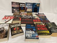 Photo of all 19 thriller and mystery novels arranged in two rows on a table, showing front covers including titles and authors.