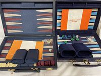 Two backgammon sets with checkers, dice, cups and rules booklets displayed inside their hard cases.