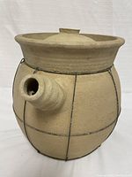 Side view of the round vintage sand clay pot showing the spout and metal wire reinforcement.