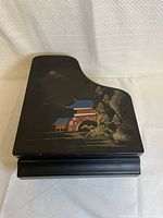 Closed view of black lacquer jewelry box shaped like a grand piano showing Asian landscape design on lid.