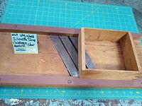 Top view of the wooden Silvretta cabbage slicer mandolin with three visible cutting blades and sliding tray box with dovetail corners, placed on a green grid cutting mat with a label.