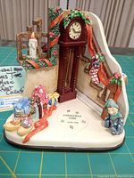 Front angle view of vintage Goebel Hummel Christmas Time 2016 Musikfest porcelain figurine featuring grandfather clock, decorated stair banister, and children playing with toys.