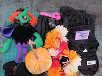 Overview of all items in the lot including stuffed witch doll, black hooded cape, black apron with pink strap, fabric pumpkin, and flower crown accessory.