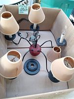 Full view of the lamp showing five light arms with beige tapered shades, central red apple shape base, black arms, and chain.