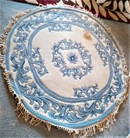 Top-down image of the vintage blue and ivory round wool rug with fringe, showing central floral medallion and scrolling designs.