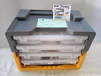 Photo of the black and yellow plastic storage case with four transparent drawers stacked and closed, showcasing the carrying handle on top.