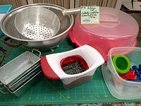 Photo of the colander, loaf pans, KitchenAid apple slicer, large cake carrier container, and a container with chip bag clips, showing the main items in the lot.