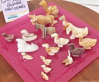 Shows array of miniature alabaster and marble animal figurines arranged on red tray, includes duck, horse, dog and other animals in polished stone with natural veining and colors.