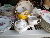 Full set of Meissen Flower Poland porcelain dinnerware with floral pattern and scalloped edges, stacked and displayed on shelf.