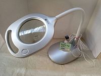 Full view of the white desk magnifying lamp with flexible neck, magnifying glass, light, and base in a corner setting.