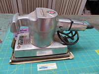 Side view of the Rockwell sander showing metal body, handle, cord, and sanding surface.