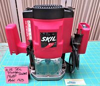 Front view of Skil 1 3/4 HP plunge base router, showing red body with black top and handles, measurement scale on side and power cord.