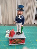 Front view of vintage cast iron Uncle Sam coin bank with red money bag on a green cutting mat.