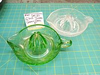 Two glass citrus juicers side by side on a green grid surface; green and clear glass with 8 inch diameter noted on card.