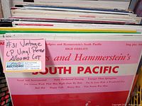 Photo of the vintage vinyl LP records stacked vertically, showing the label #31 Vintage LP Vinyl Record Albums Lot tag and a visible album titled Rodgers and Hammerstein's South Pacific with a pink cover.