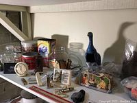 Overall arrangement of vintage jars, tins, matchbox, duck figurine, clock, and other collectibles on white surface.