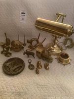 Photo showing all brass items arranged on a quilted white cover: adjustable lamp, musical train, animal figures, trinket box.
