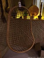 Full side view of wicker hanging chair suspended indoors with woven textured background.