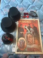 Full lot showing three black top hats, one black Chinese style hat, two red bow ties, one black bow tie, and packaged Houdini poster on a mattress.