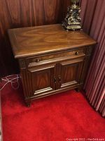Front and angled view of one vintage wooden nightstand showing drawer and cabinet doors with brass pulls and carved wood accents